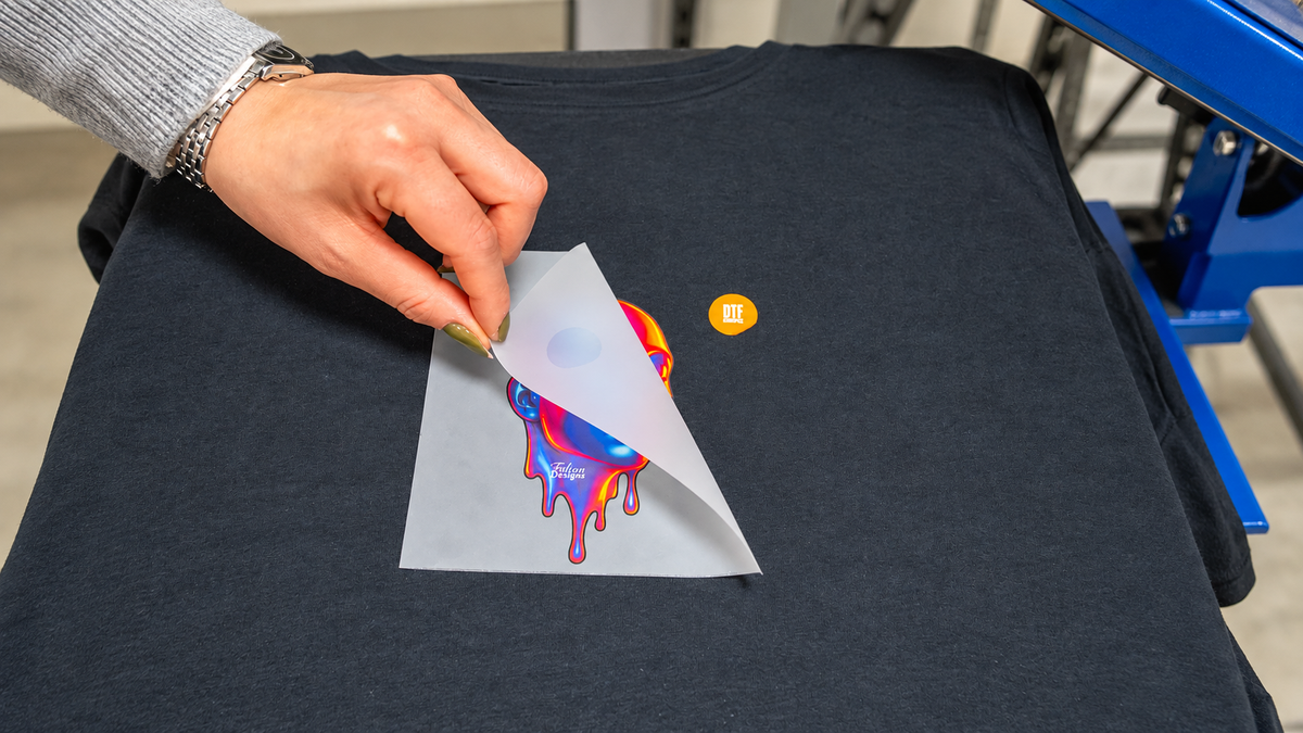 Carrier film being peeled from a DTF print on a charcoal garment